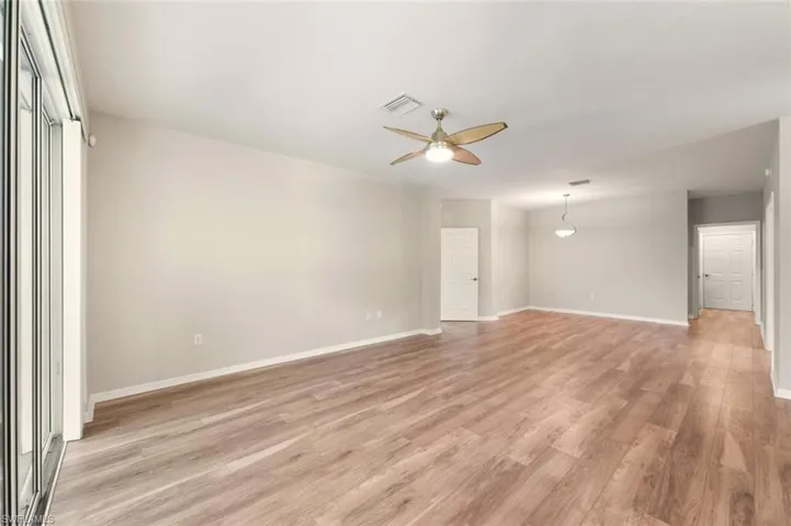 Expansive open-concept room featuring wood-finish flooring, light neutral wall paint, and a modern ceiling fan
