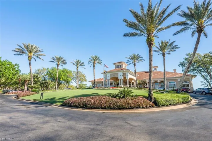 Grand building exterior featuring a tile roof, arched entryway, extensive landscaping, and mature palm trees