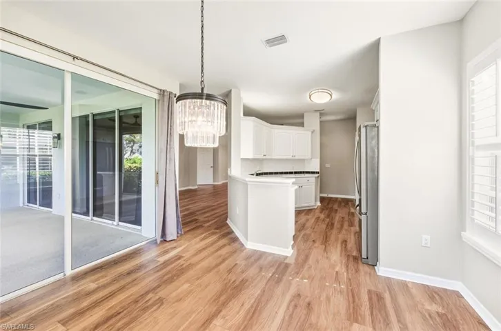 Spacious dining area featuring wood-finish flooring, a tiered chandelier, and direct access to a screened patio through large sliding glass doors