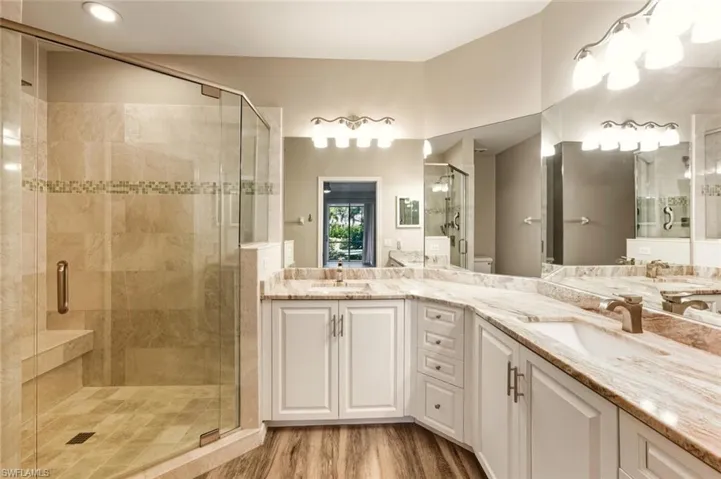 Expansive bathroom featuring a glass-enclosed shower with a built-in bench, dual vanity sinks, extensive counter space, and wood-finish flooring