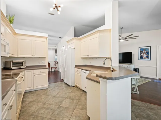 Kitchen with dark countertops, white appliances, a peninsula, a kitchen breakfast bar, and a ceiling fan