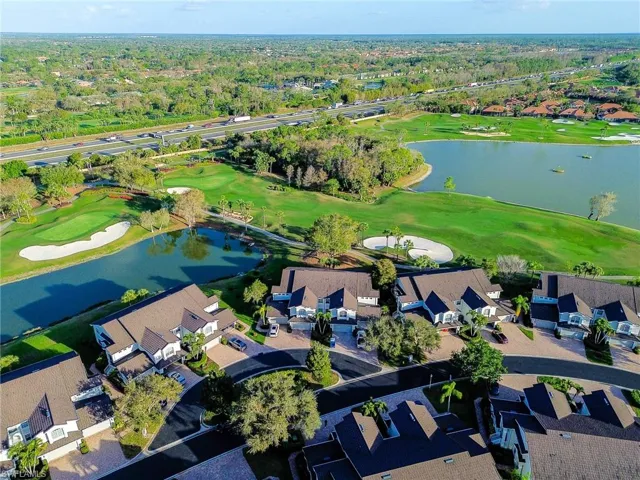 Aerial view of property and surrounding area featuring a golf course, nearby suburban area, and a large body of water