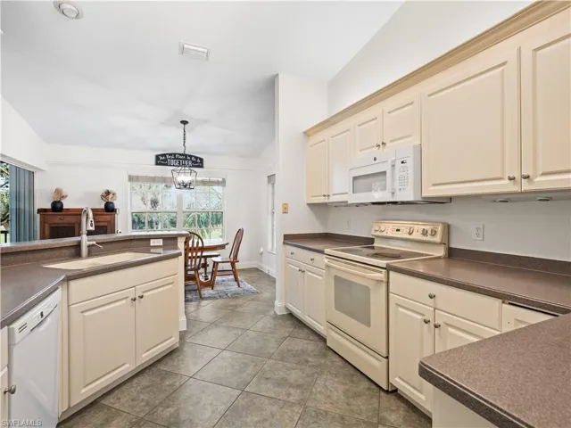 Kitchen with white appliances, dark countertops, a chandelier, and dark tile patterned flooring