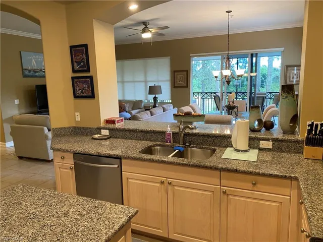 Kitchen featuring open floor plan, crown molding, dark stone countertops, hanging lights, and a ceiling fan