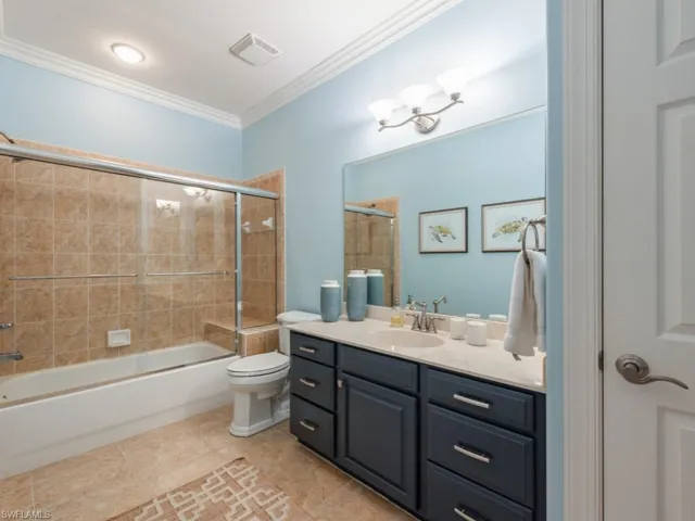 Full bathroom with vanity, tile patterned flooring, crown molding, toilet, and enclosed tub / shower combo