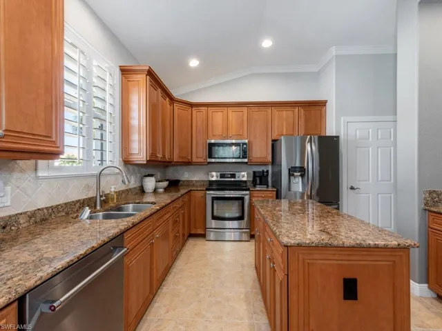 Kitchen with tasteful backsplash, light tile patterned floors, stainless steel appliances, a kitchen island, and lofted ceiling