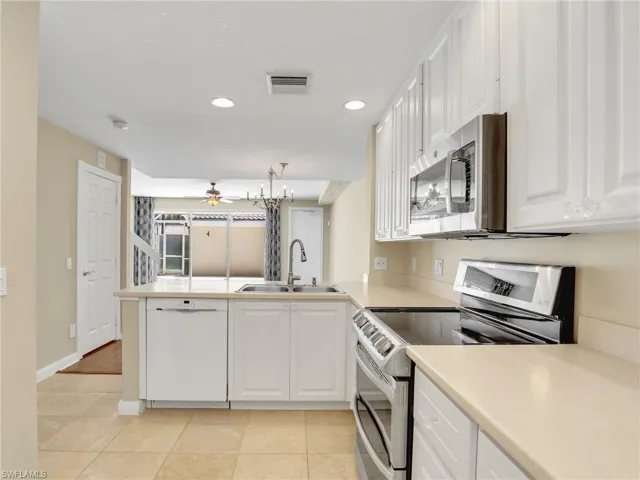 Kitchen with stainless steel appliances, a sink, ceiling fan, a peninsula, and white cabinetry