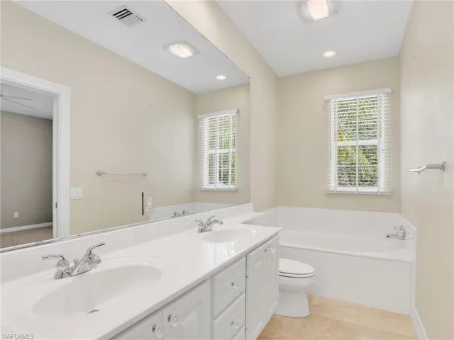 Bathroom featuring a bath, toilet, double vanity, and recessed lighting