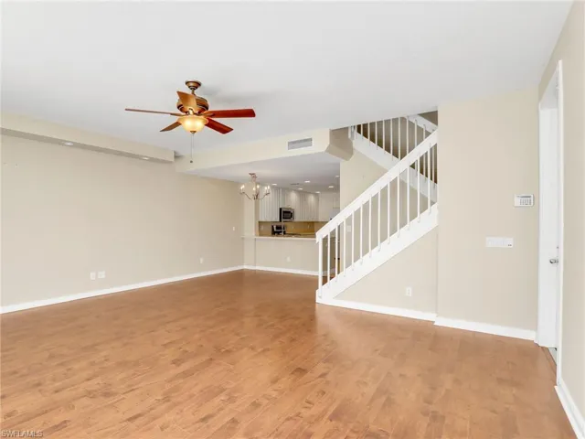 Unfurnished living room featuring a chandelier, light wood-style floors, stairs, and ceiling fan