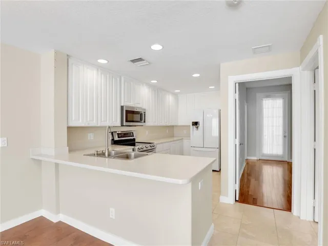 Kitchen featuring stainless steel appliances, a peninsula, light countertops, baseboards, and white cabinetry