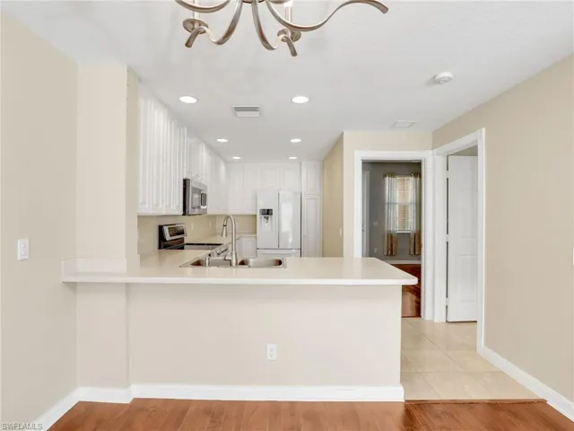 Kitchen with stainless steel appliances, a sink, a peninsula, a chandelier, and light countertops