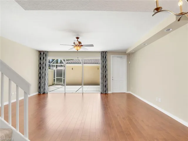 Unfurnished living room featuring ceiling fan, baseboards, wood finished floors, and stairway