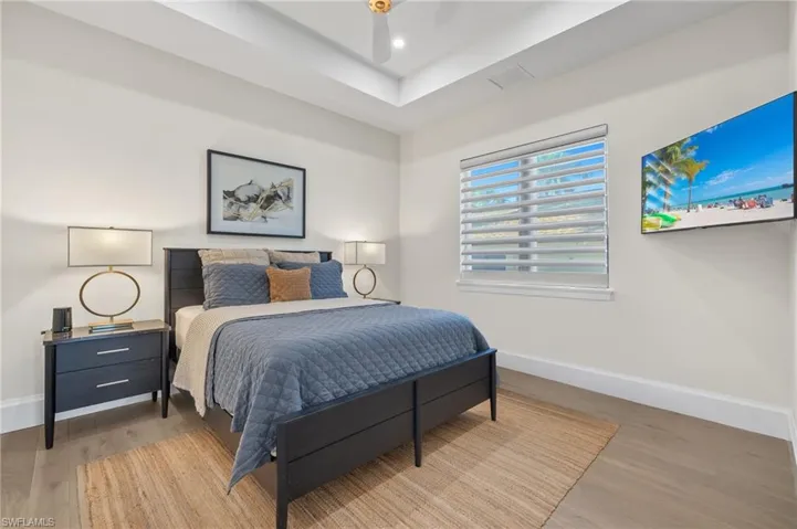 Bedroom with baseboards, wood finished floors, a raised ceiling, and recessed lighting