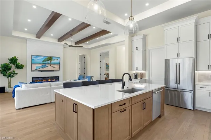Kitchen featuring appliances with stainless steel finishes, a sink, light wood finished floors, open floor plan, and beam ceiling