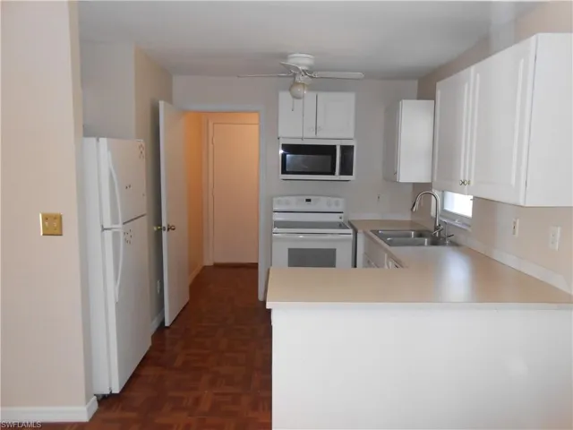 Kitchen featuring white appliances, light countertops, white cabinets, parquet floors, and a ceiling fan