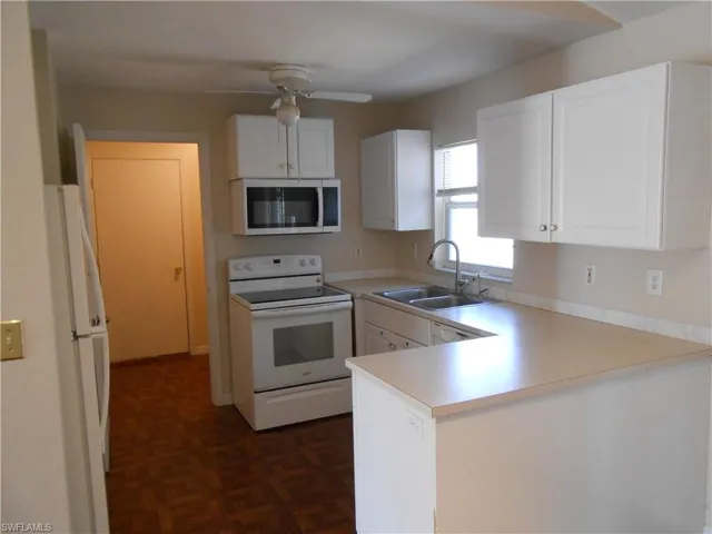 Kitchen with white appliances, white cabinetry, a peninsula, light countertops, and parquet floors