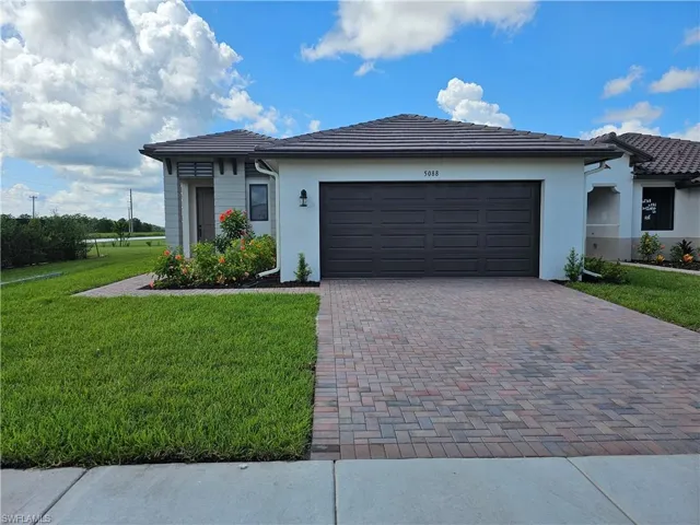 Prairie-style house featuring decorative driveway, a front yard, a tiled roof, stucco siding, and an attached garage