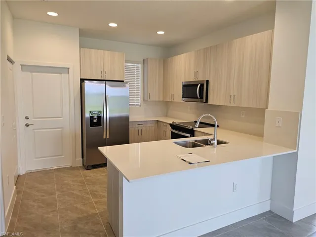Kitchen featuring stainless steel appliances, a peninsula, light tile patterned flooring, light brown cabinetry, and modern cabinets