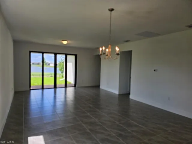 Empty room with a chandelier, dark tile patterned floors, and a water view