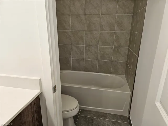 Bathroom with dark tile patterned flooring, vanity, and bathtub / shower combination
