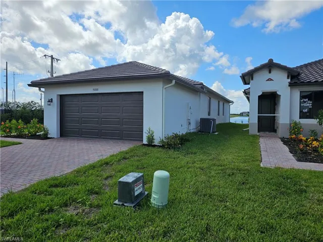 View of property exterior with stucco siding, a lawn, decorative driveway, an attached garage, and a tiled roof