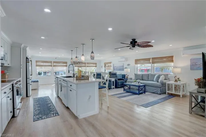 Kitchen with white cabinetry, white appliances, open floor plan, a kitchen island with sink, and light wood finished floors
