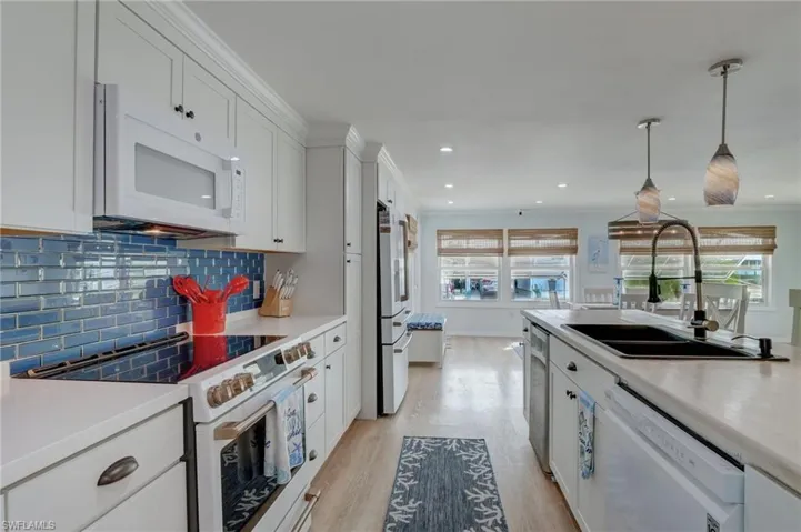 Kitchen with white appliances, white cabinetry, light countertops, light wood finished floors, and ornamental molding