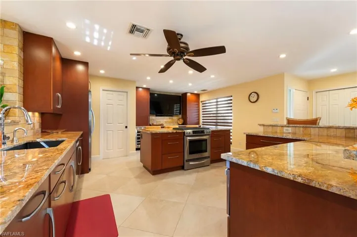 Kitchen featuring decorative backsplash, light stone counters, stainless steel appliances, a ceiling fan, and light tile patterned floors