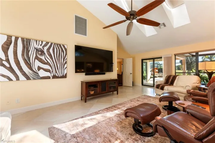 Living area with vaulted ceiling, ceiling fan, a skylight, and tile patterned floors