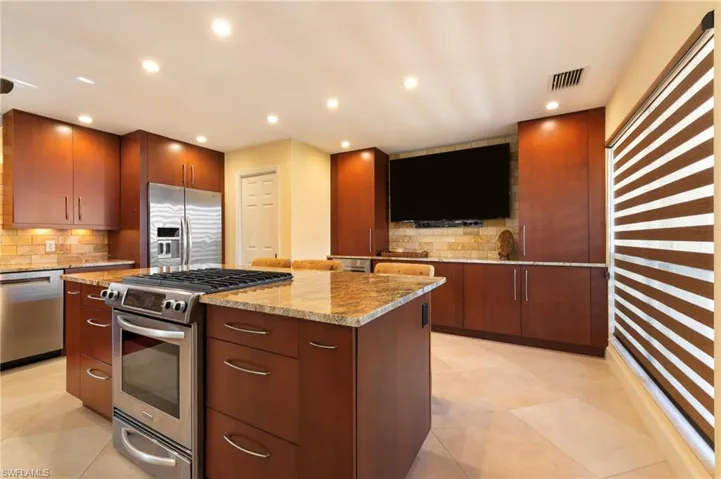 Kitchen with stainless steel appliances, light stone countertops, recessed lighting, a center island, and backsplash