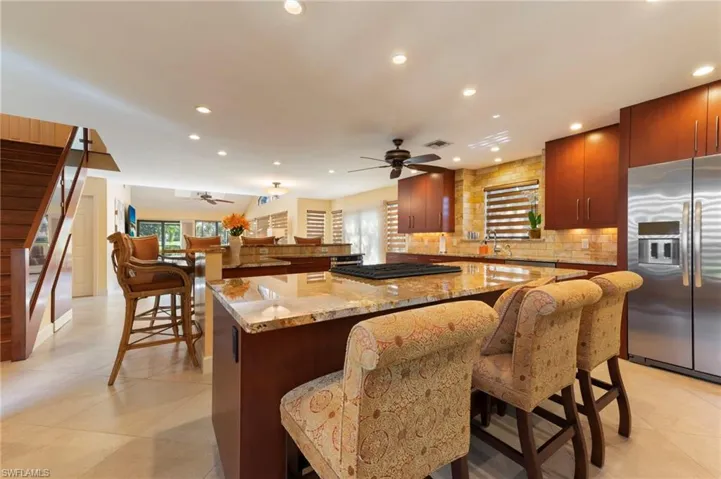 Kitchen with light stone countertops, a kitchen breakfast bar, stainless steel refrigerator with ice dispenser, recessed lighting, and tasteful backsplash