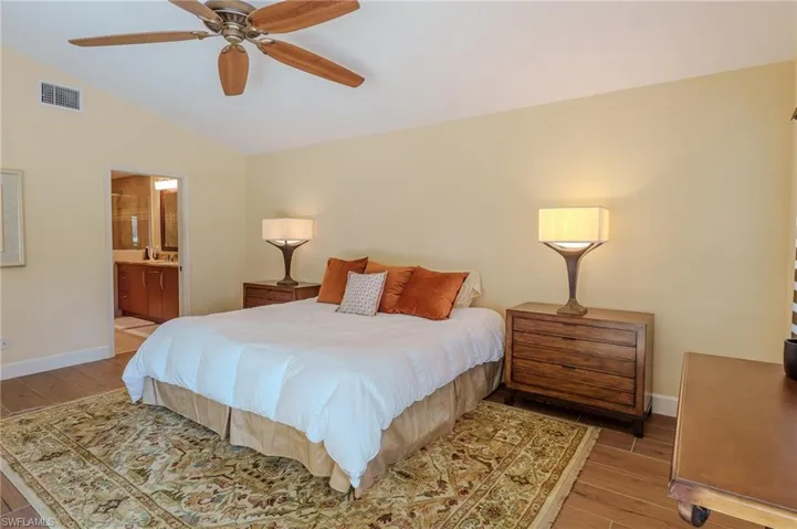 Bedroom featuring vaulted ceiling, wood finished floors, ceiling fan, and ensuite bathroom