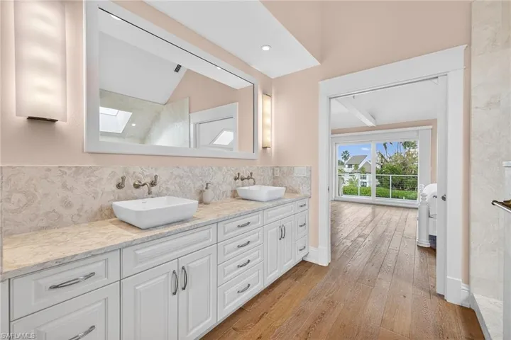 Full bath featuring double vanity, a skylight, light wood-type flooring, and decorative backsplash
