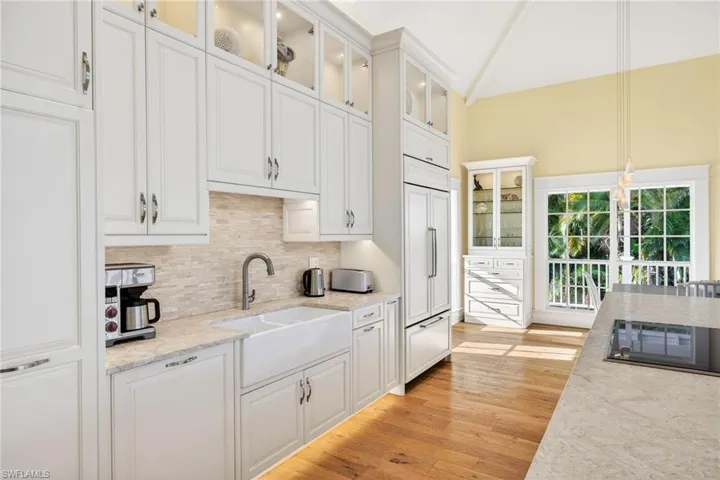Kitchen featuring glass insert cabinets, white cabinets, decorative light fixtures, light stone counters, and high vaulted ceiling