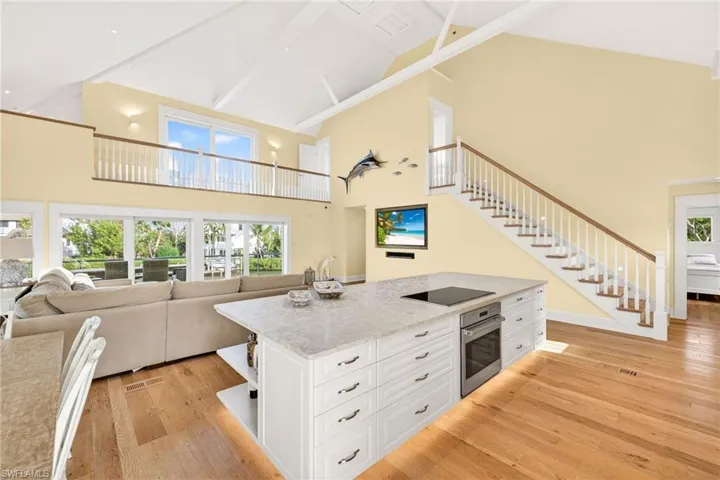 Kitchen with open shelves, white cabinets, light stone countertops, a center island, and high vaulted ceiling