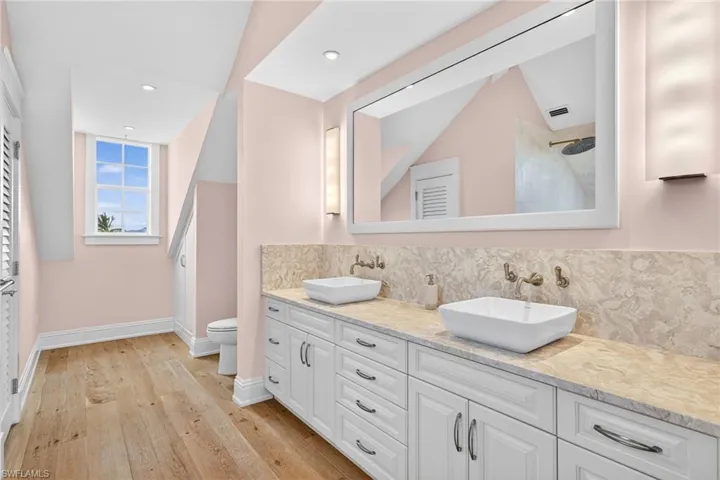 Bathroom with double vanity, light wood-type flooring, a shower, recessed lighting, and backsplash