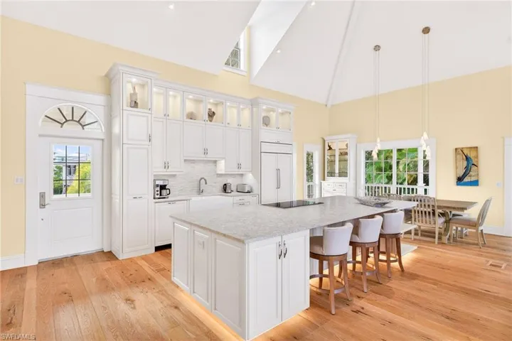 Kitchen with high vaulted ceiling, white cabinets, glass insert cabinets, hanging light fixtures, and light stone counters