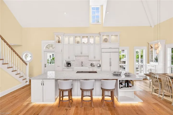 Kitchen with white cabinets, glass insert cabinets, open shelves, backsplash, and high vaulted ceiling