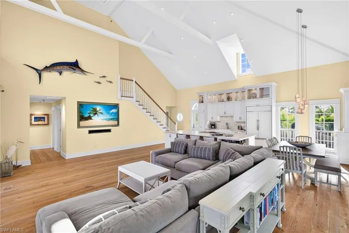 Living area with high vaulted ceiling, light wood-style floors, and stairs