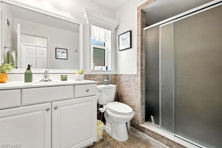 Bathroom featuring a white vanity with integrated sink, a large framed mirror, and a tiled shower with frosted glass doors