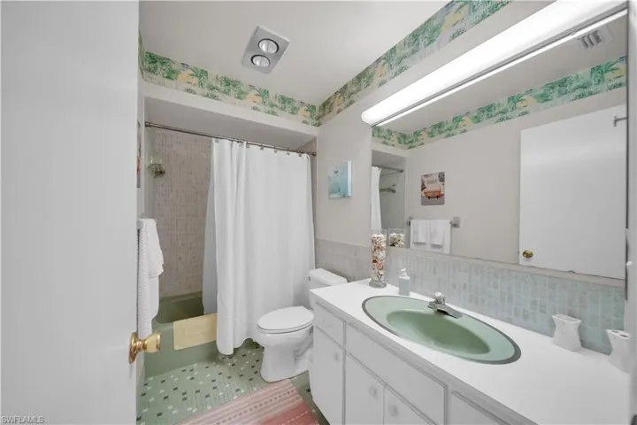 Bathroom featuring a green tub, patterned floor tiles, a vanity with a green sink, and a large wall-mounted mirror