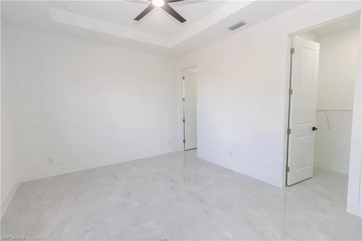 Bedroom with a raised ceiling, a walk in closet, and a ceiling fan