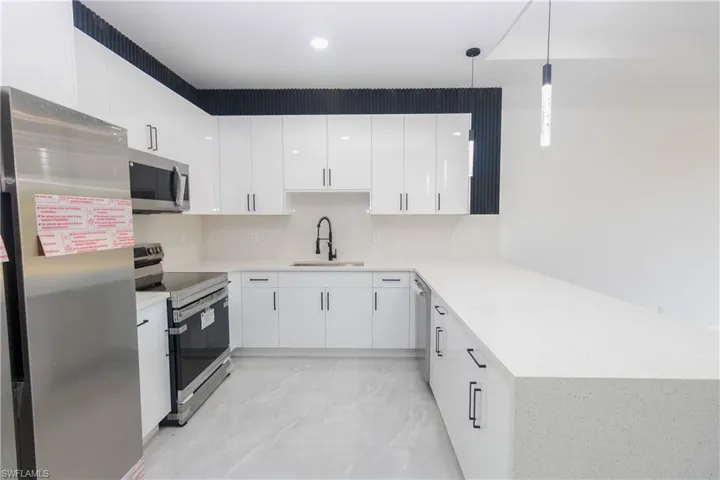 Kitchen featuring stainless steel appliances, white cabinets, a peninsula, and decorative light fixtures