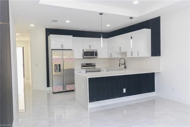 Kitchen featuring hanging light fixtures, stainless steel appliances, white cabinets, a peninsula, and light stone countertops