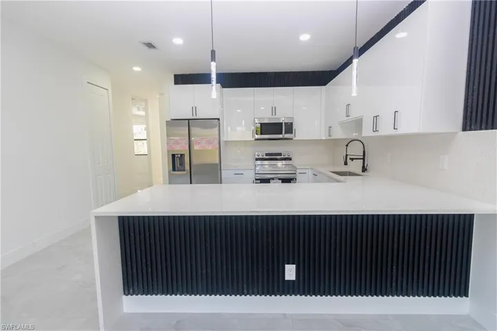 Kitchen with stainless steel appliances, a peninsula, light stone countertops, and white cabinetry