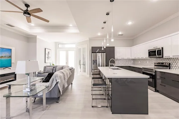 Kitchen with stainless steel appliances, a kitchen island with sink, sink, white cabinets, and hanging light fixtures
