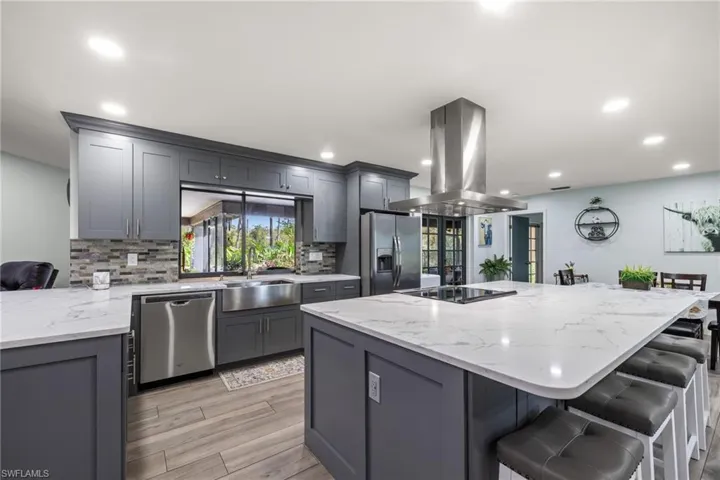 Kitchen with gray cabinets, a center island, island range hood, and appliances with stainless steel finishes