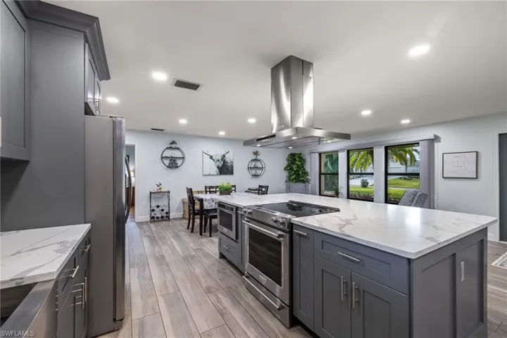 Kitchen featuring light stone countertops, range hood, light hardwood / wood-style floors, gray cabinets, and appliances with stainless steel finishes