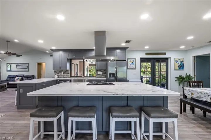 Kitchen with a center island, tasteful backsplash, stainless steel fridge, gray cabinets, and island range hood
