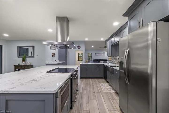 Kitchen with island exhaust hood, kitchen peninsula, light hardwood / wood-style floors, gray cabinets, and appliances with stainless steel finishes